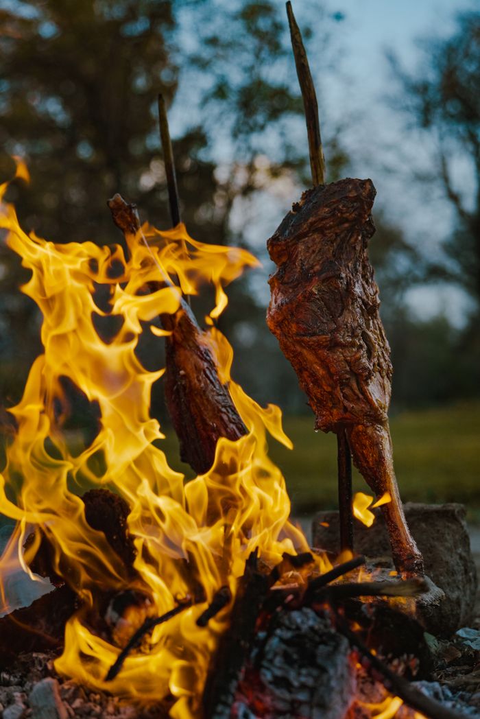Delicious roasted meat cooked over an open wood-fired flame outdoors.